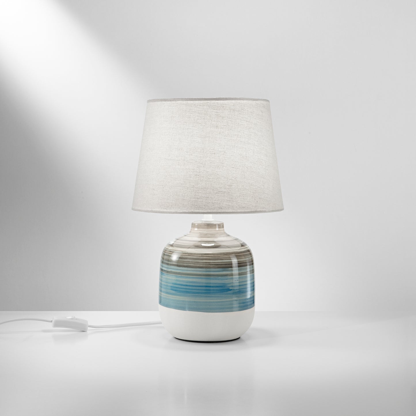 Lume APACHE con base in ceramica e paralume in tessuto bianco.